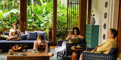 A family is captured while unwinding on the patio of a tropical resort filled with vibrant, handcrafted furniture, wooden accents, and lush greenery.