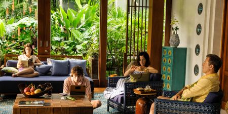 A family is captured while unwinding on the patio of a tropical resort filled with vibrant, handcrafted furniture, wooden accents, and lush greenery.