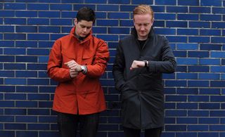 Two men wearing jackets looking at their wrist watch