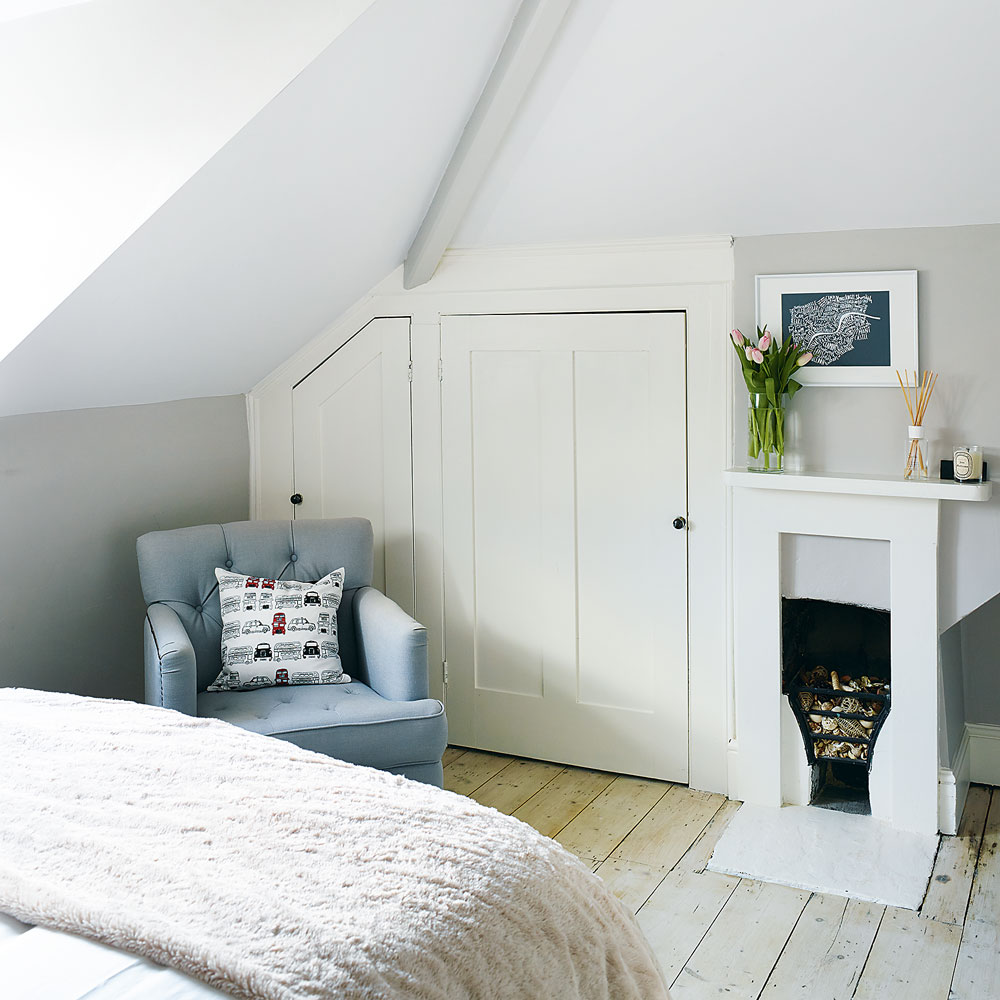 Small attic bedroom with built in cupboards beside a fireplace and blue chair