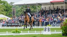 Emily King rides bay horse Valmy Biats in canter towards the camera in the Badminton Horse Trials dressage arena with the packed stands behind.