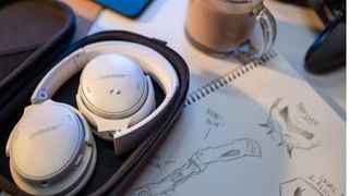 Bose QuietComfort 45 folded in their carry case next to a sketchpad and mug