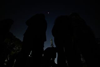 people gather around telescopes and look up at a blood red moon during the total lunar eclipse.