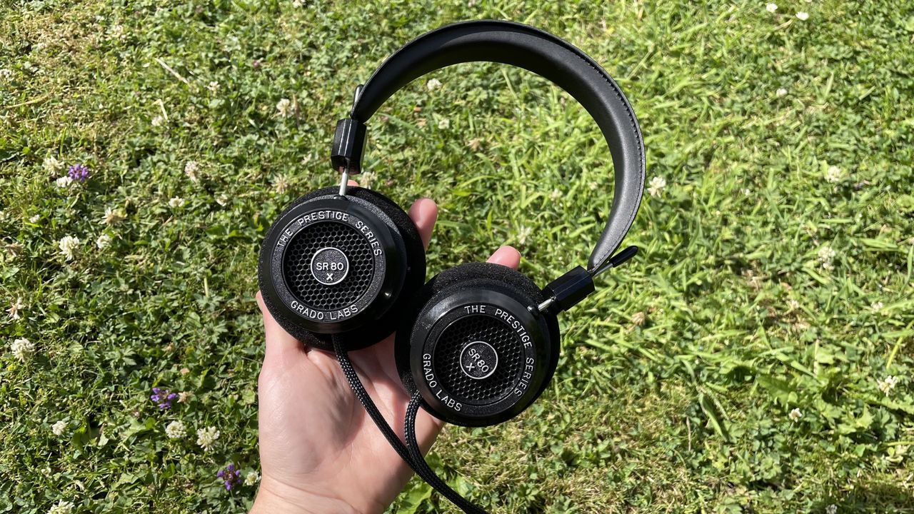 Becca's hand holding the Grado SR80x headphones against some grass