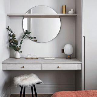 Dressing table in gray alcove with circular wall mirror and fur-covered stools