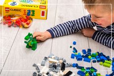 child playing with LEGO set - he's made a green dinosaur and is playing on the floor