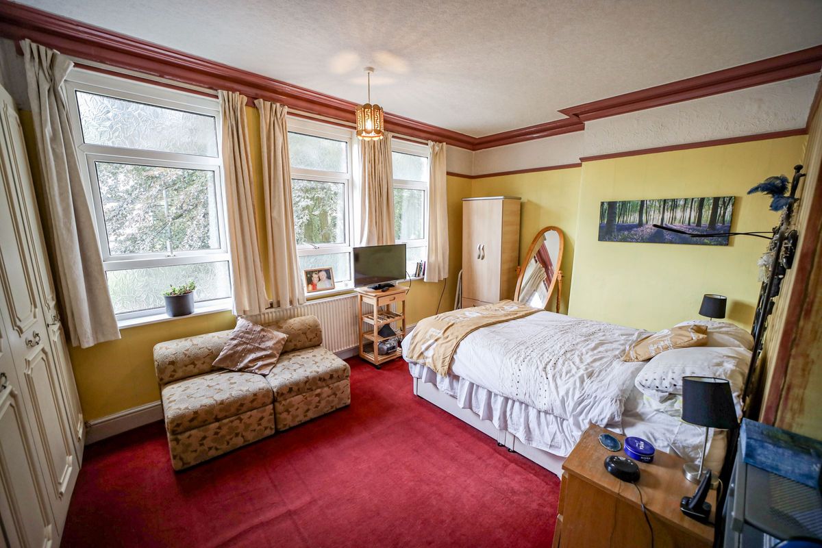 A red carpeted bedroom with 3 large windows and a high ceiling