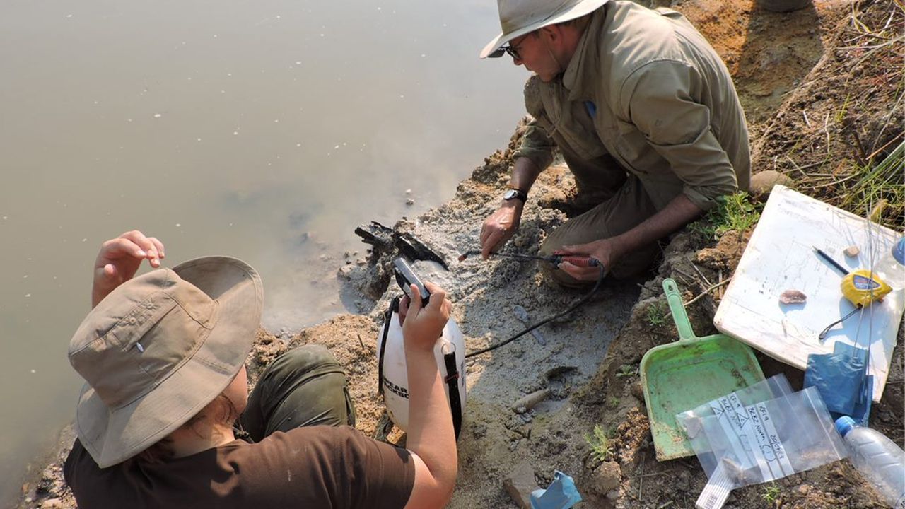 Professor Larry Barham (pictured, right) uncovering the wooden structure on the banks of the river with a fine spray.