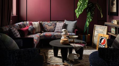 patterned sofa in a cozy living room with purple walls, coffered ceiling, patterned carpet, potted plant, gallery wall, and round black coffee table with vases on it