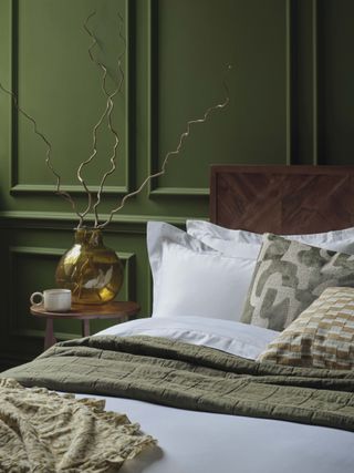 A green panelled bedroom with a dark wood bed and white sheets