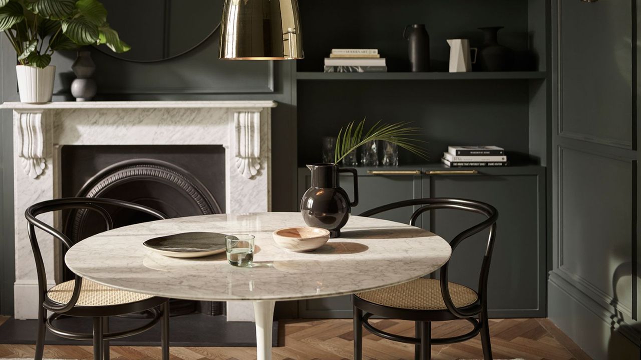 A dark dinign room with black walls, a white round table with two black chairs, and a white fireplace surround 