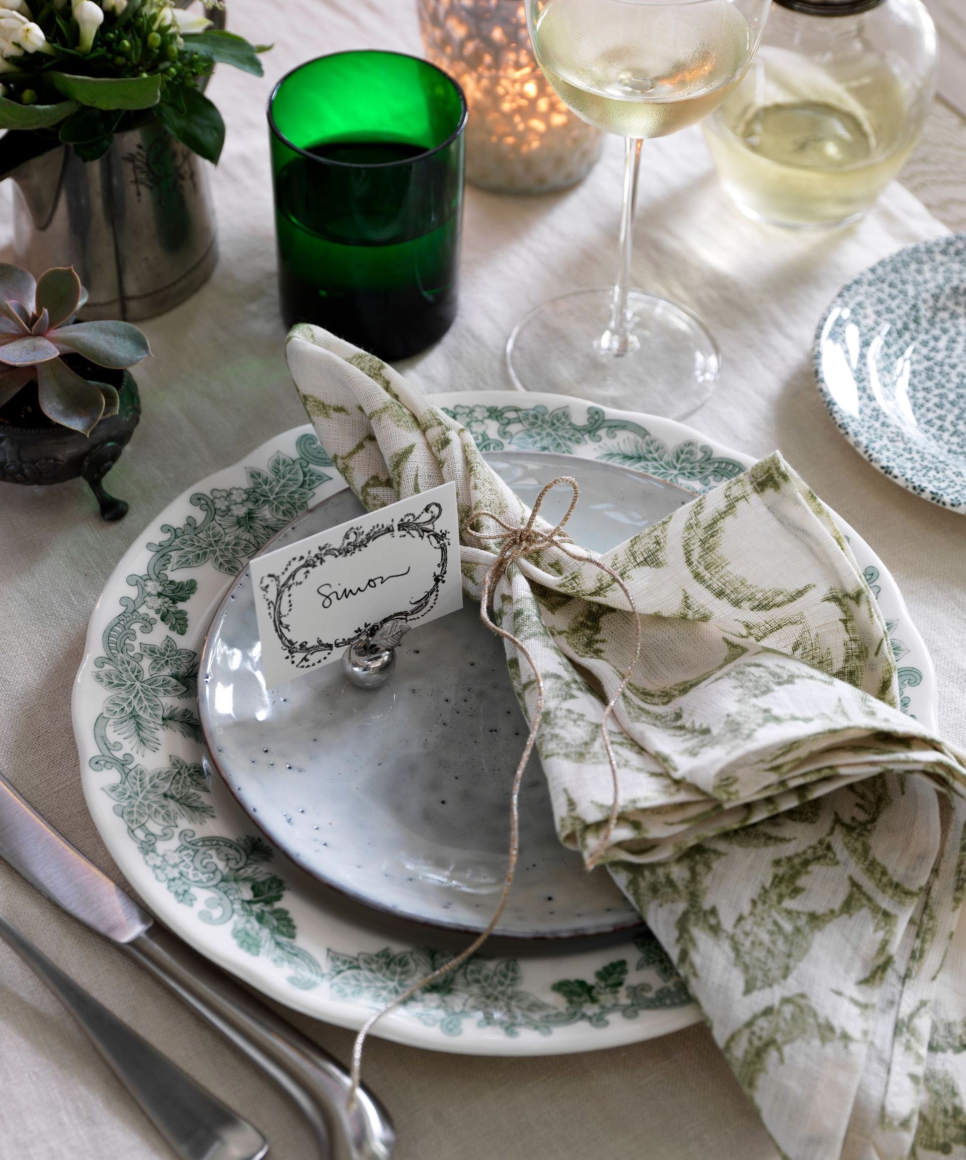 Stamped place card on a place setting with green and white plates and a napkin tied with brown string featuring delicate prints