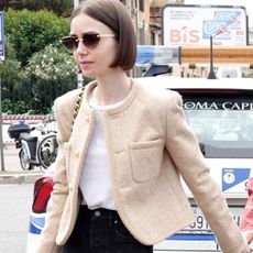 Lily Collins with her husband Charlie McDowell attending the Italian Open in Rome wearing a tan Chanel jacket and black bag with black jeans and sandals.