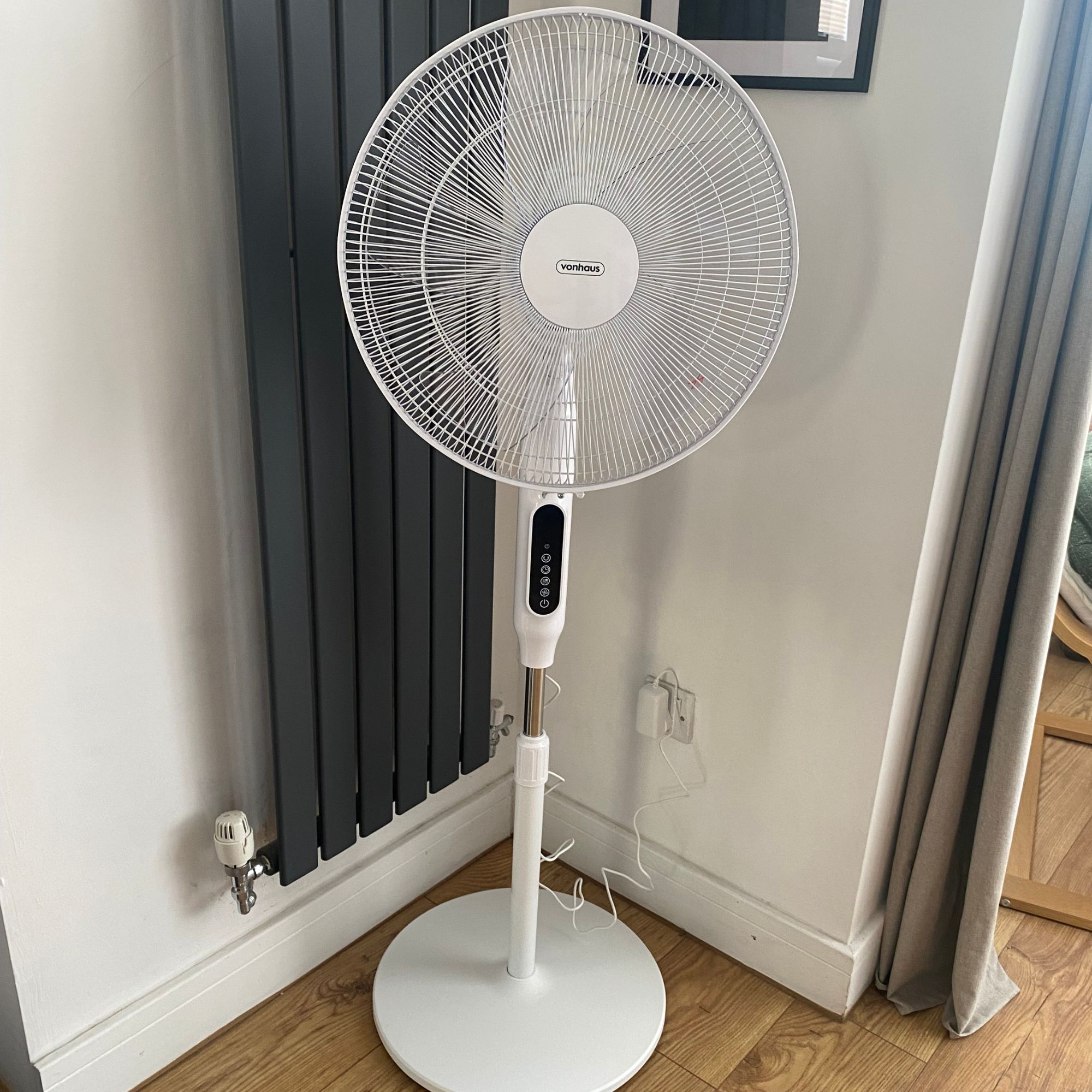 Vonhaus 16'' pedestal fan at mid-height in a corner of a room next to a dark grey vertical radiator