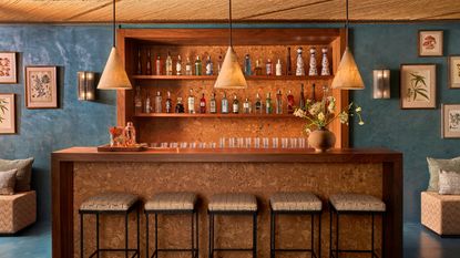 Interior shots of a turquoise plaster-tinted restaurant with textural walls and earthy furnishings throughout, from leathery banquettes and cream tablecloths to wooden accents, pendant lighting, and a rattan and wood ceiling.