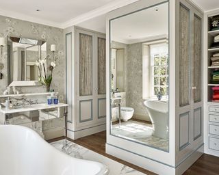 Walk-in wardrobe ideas in a scheme with gold and beige wallpaper, panelled walls and cupboards and a large mirror.