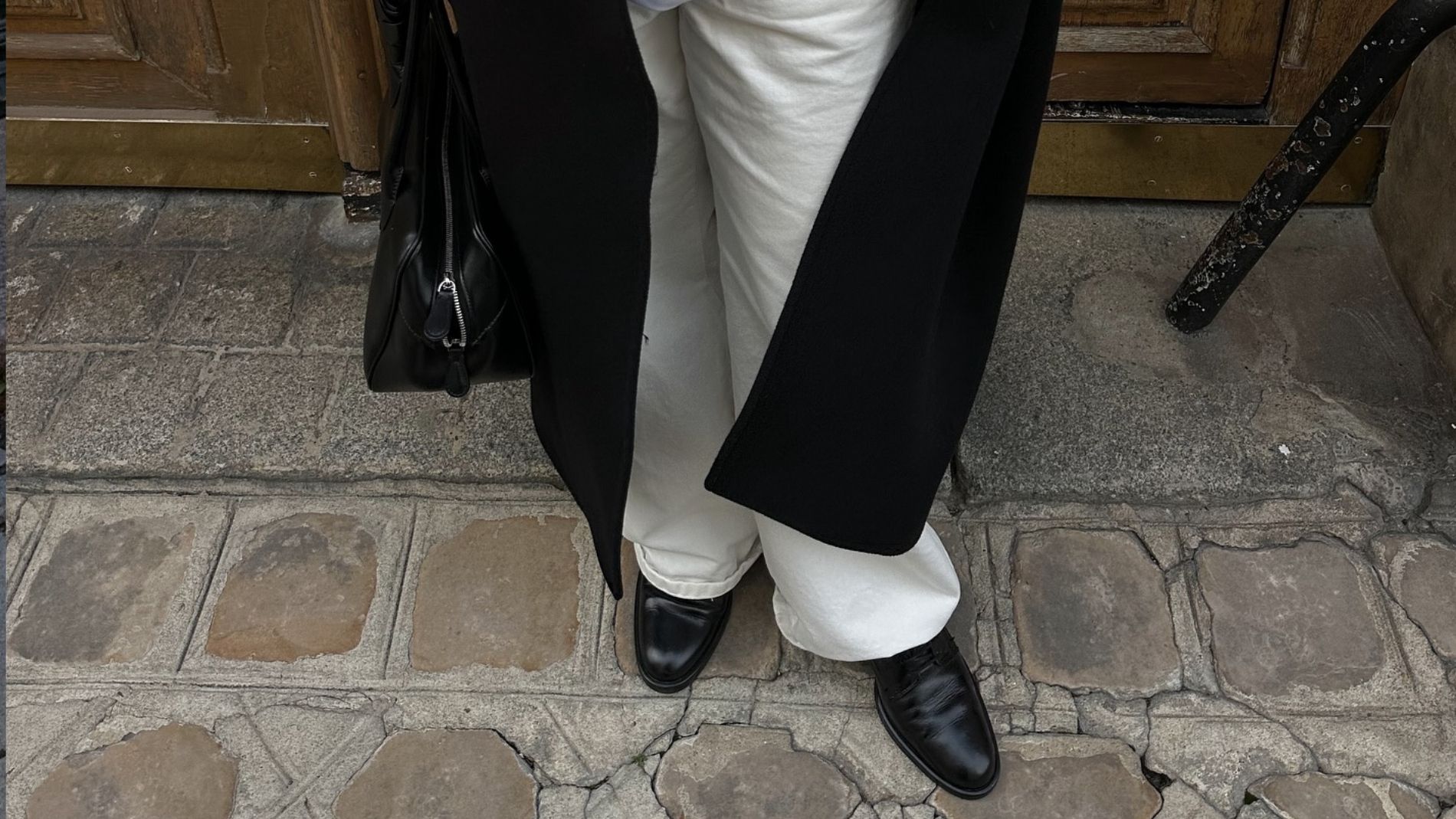 A woman wears smooth leather loafers with white pants and a black overcoat