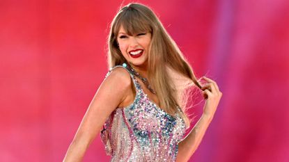 Taylor Swift wearing a sequined bodysuit and playing with her hair smiling against a pink background