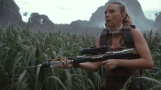 Scarlett Johansson cautiously holds a gun while standing in long grass in Jurassic World Rebirth.