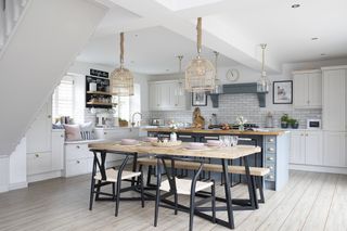 Kitchen-diner with blue Shaker-style island, black and wood dining table and chairs, rattan pendant lights and wooden floor