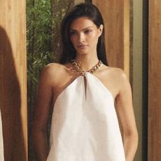 A model wearing a white dress with a gold chain around her neck from Karen Millen.