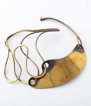 Gold curved necklace against a grey background