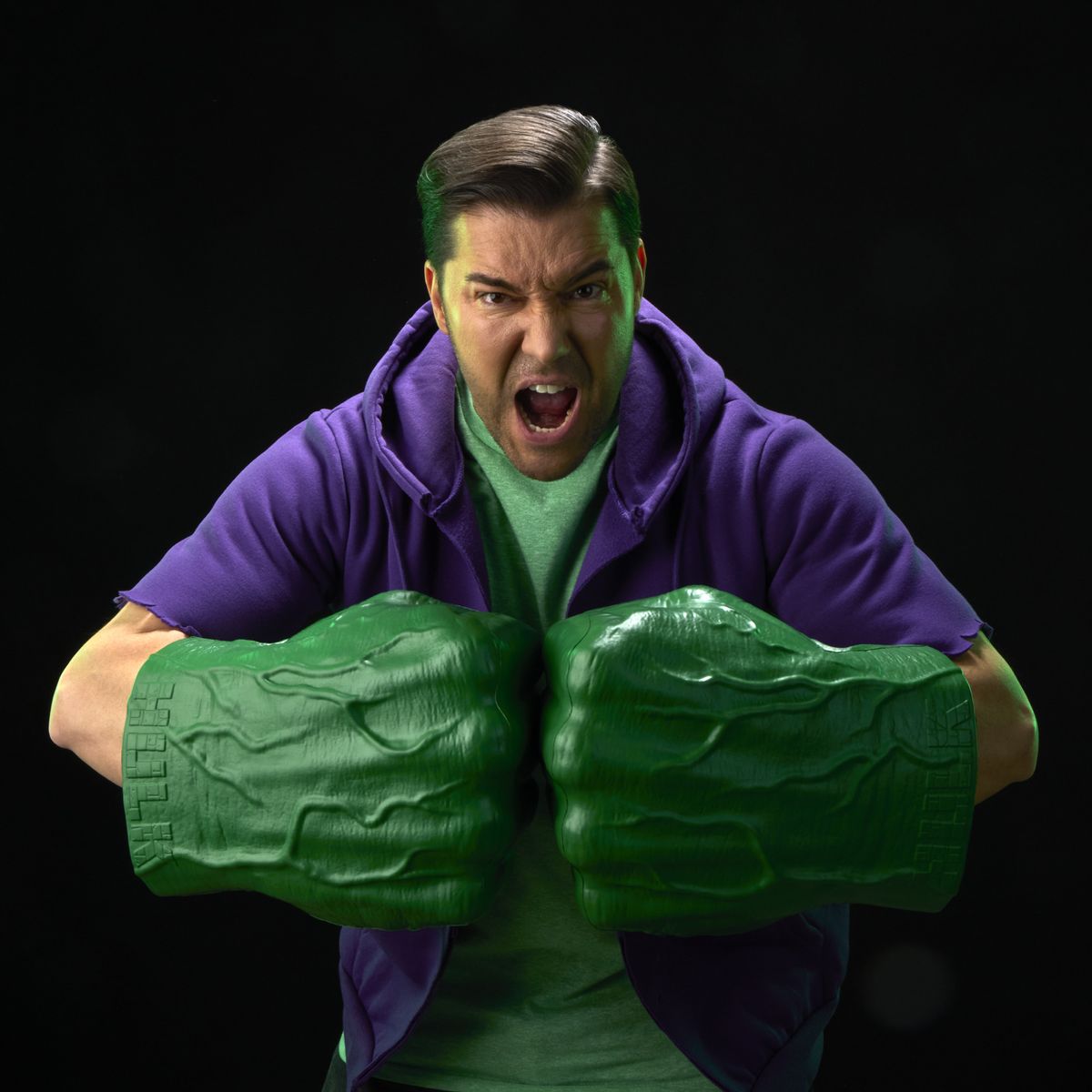 A roaring man with two Hulk Fists pretends to punch with them against a black background