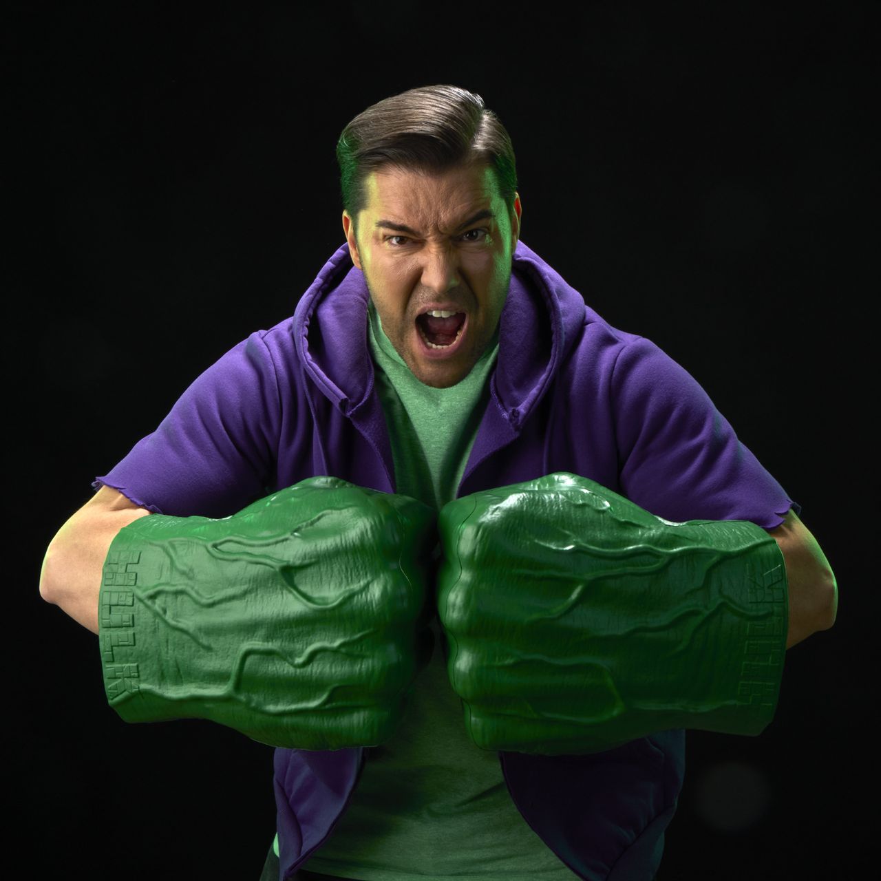 A roaring man with two Hulk Fists pretends to punch with them against a black background