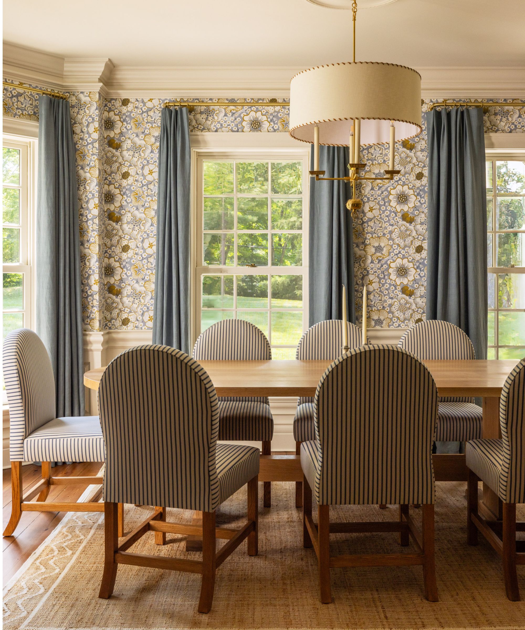 Traditional dining room with floral wallpaper, blue curtains, long curtains, wood dining table and striped blue and white chairs