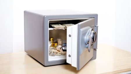 A home safe sitting on a desk with jewelry and coins inside. 
