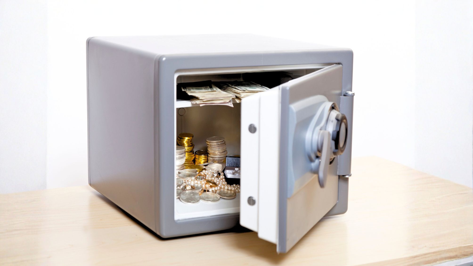 A home safe sitting on a desk with jewelry and coins inside. 