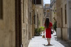 Young woman, wearing red dress, explores colourful, narrow streets in old town, Rabat, Malta.