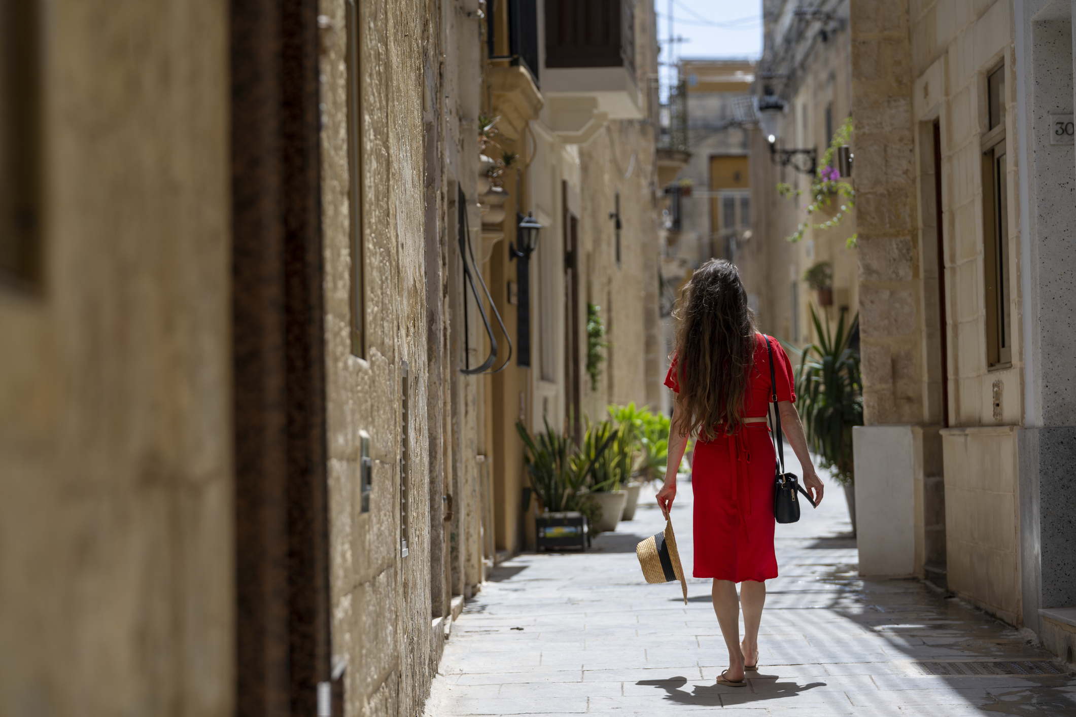 Young woman, wearing red dress, explores colourful, narrow streets in old town, Rabat, Malta.