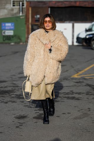 woman wearing a faux fur coat, a skirt, boots, and a bag