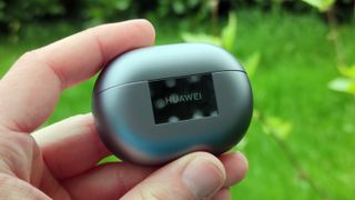 The Huawei FreeBuds Pro 3 being held in a hand above a grassy field.