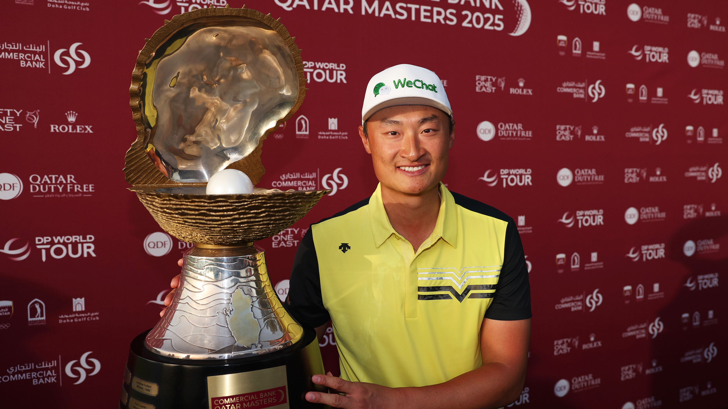 Haotong Li poses and smiles next to the Qatar Masters trophy after winning in 2025