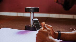Man holding plank position looks at timer on smartphone, propped up on dumbbell