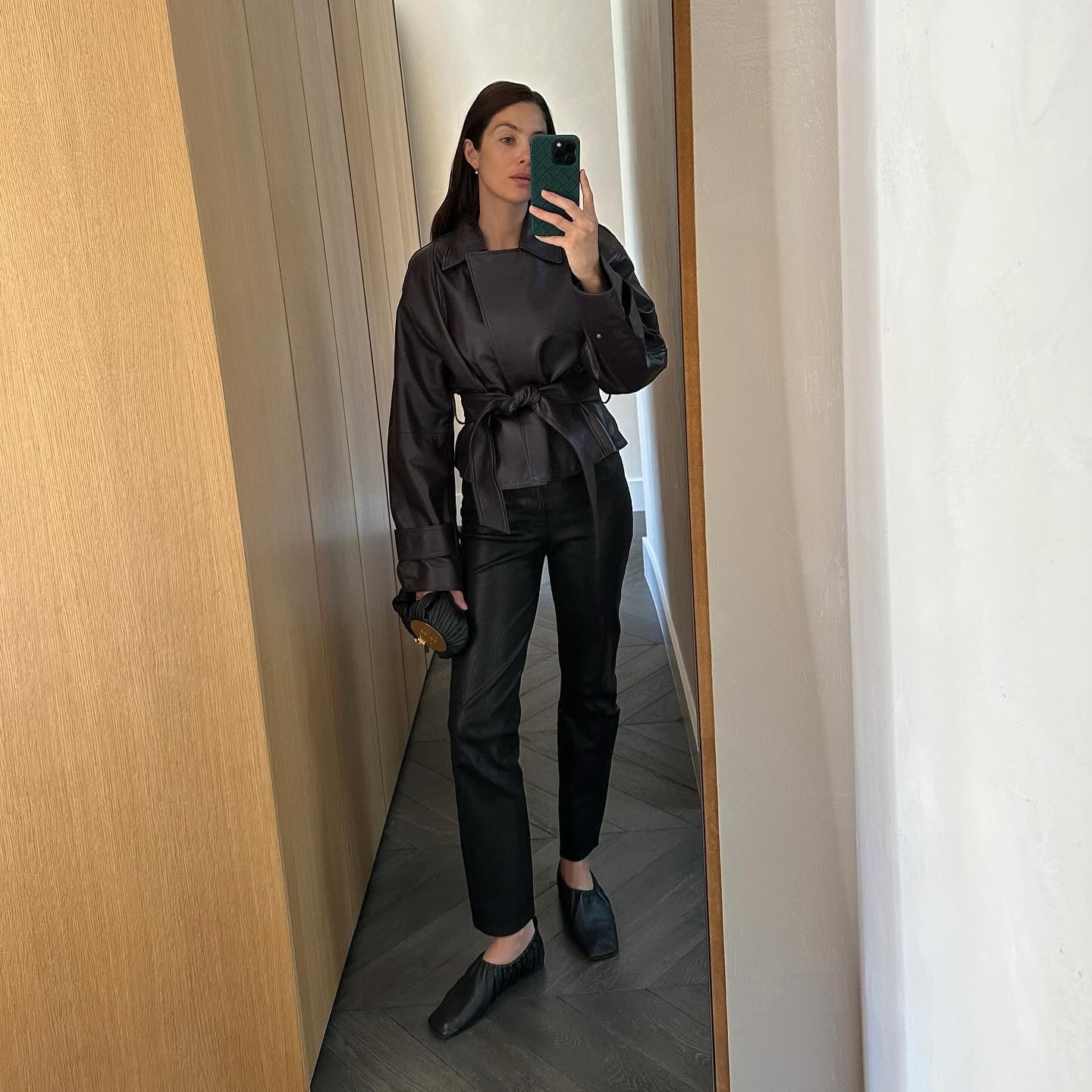 Woman wears black cigarette pants, a leather wrap coat and square toe flats. 