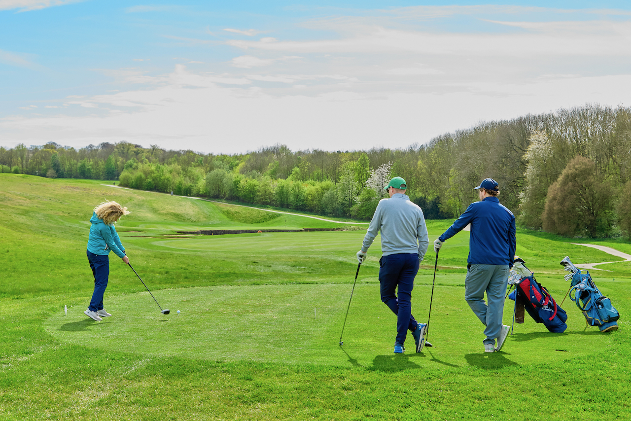 Two golfers watching another player tee off with driver