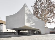 Large concrete building with curved sides, a tourist office on the ground with a tall tree behind