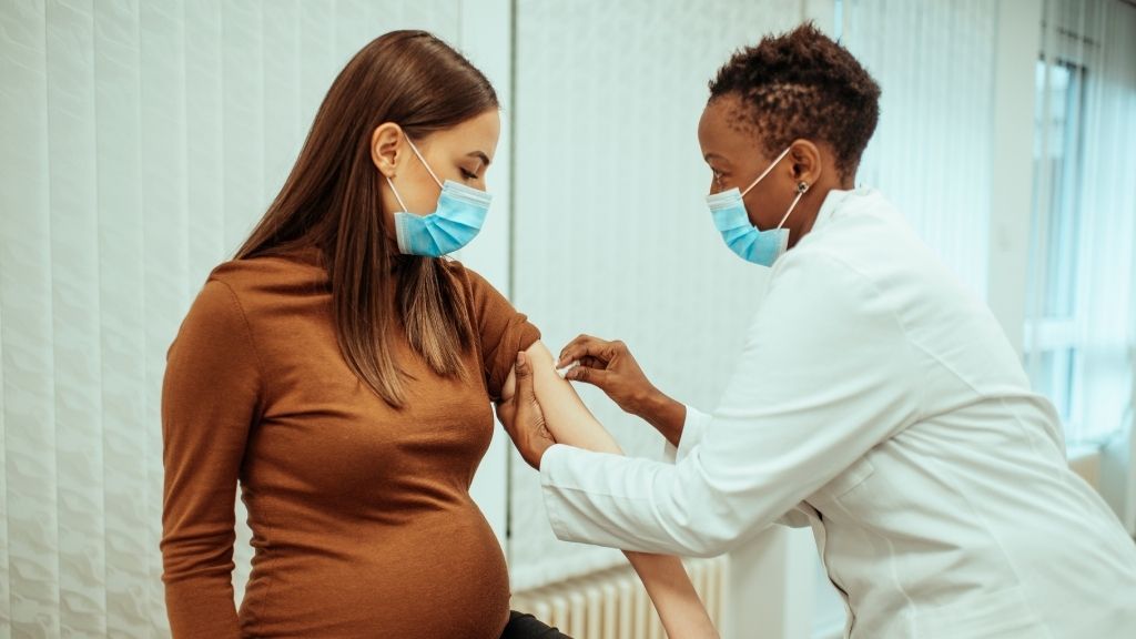 A pregnant women wearing a surgical mask receives a vaccine at the doctor&#039;s office