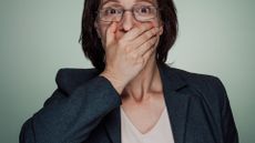 middle aged woman holds a hand over her mouth as if gasping