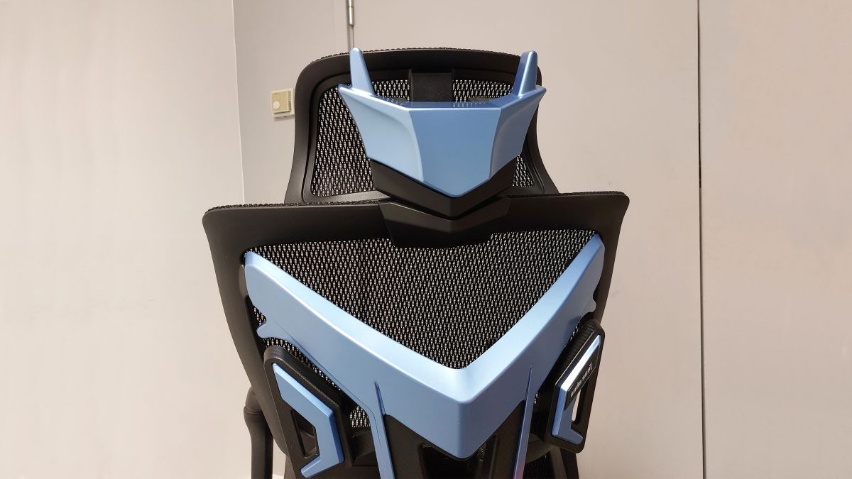 A close up of the AndaSeat X-Air Pro Mesh Office Gaming Chair. We see the chair from the back, the hefty plastic back frame prominent in the image. The back of the headrest features blue plastic that looks not unlike a robot&#039;s faceplate, with two &#039;ear&#039; antenna-like shapes jutting up from the top of the &#039;head&#039;.