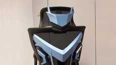 A close up of the AndaSeat X-Air Pro Mesh Office Gaming Chair. We see the chair from the back, the hefty plastic back frame prominent in the image. The back of the headrest features blue plastic that looks not unlike a robot's faceplate, with two 'ear' antenna-like shapes jutting up from the top of the 'head'.