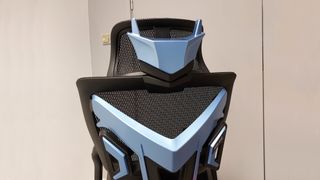 A close up of the AndaSeat X-Air Pro Mesh Office Gaming Chair. We see the chair from the back, the hefty plastic back frame prominent in the image. The back of the headrest features blue plastic that looks not unlike a robot's faceplate, with two 'ear' antenna-like shapes jutting up from the top of the 'head'.