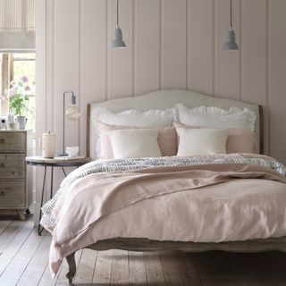 White bedroom with wall panelling, wall lights and wooden bed