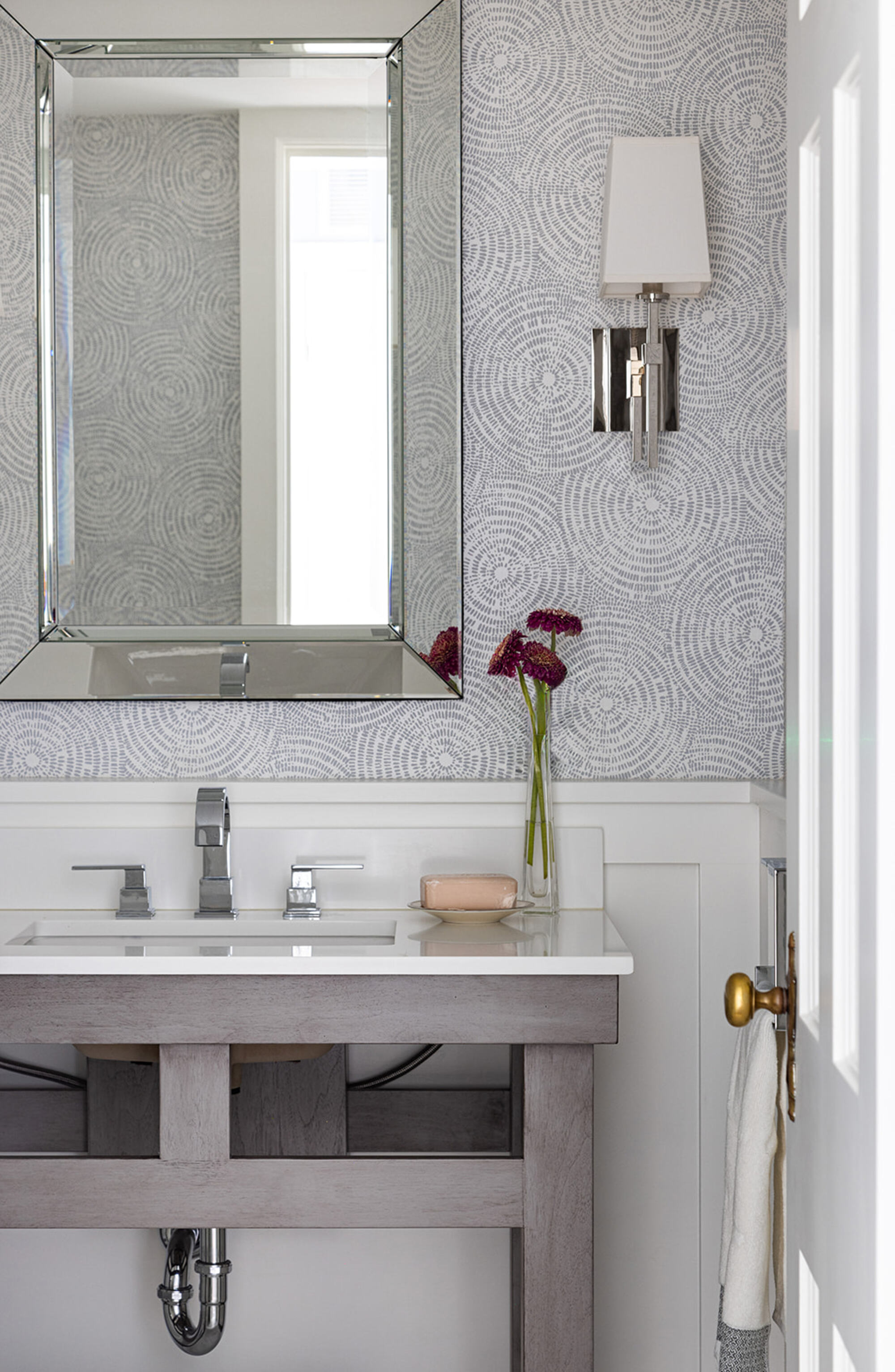 A bathroom with a vanity, mirror, and grey swirly patterned wallpaper