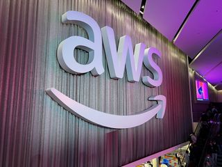The AWS logo, on a curtain-like wall at AWS re:Invent 2023 at the Venetian Hotel and Casino in Las Vegas. Decorative: The logo (the letters 'AWS' with a curved arrow beneath) is in white, and the whole photo is lit with purple lighting.