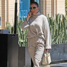 J.Lo wears a gray turtleneck sweater, gray slim-fit trousers, an hermes bag, and oversize aviator sunglasses