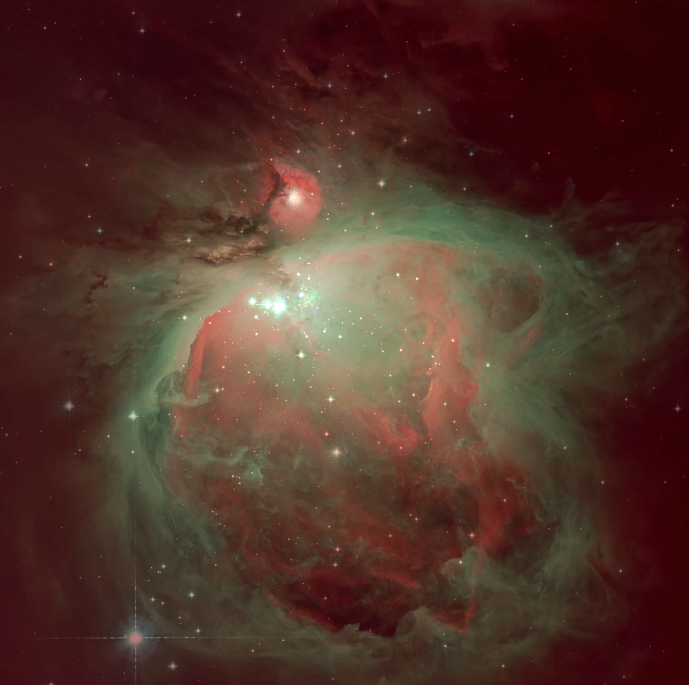 The swirling mass of interstellar dust and gas that forms the Orion Nebula is pictured glowing against the blackness of space. A collection of particularly bright stars are visible in the center of the nebula, surrounded by a radiation-sculpted cavity.